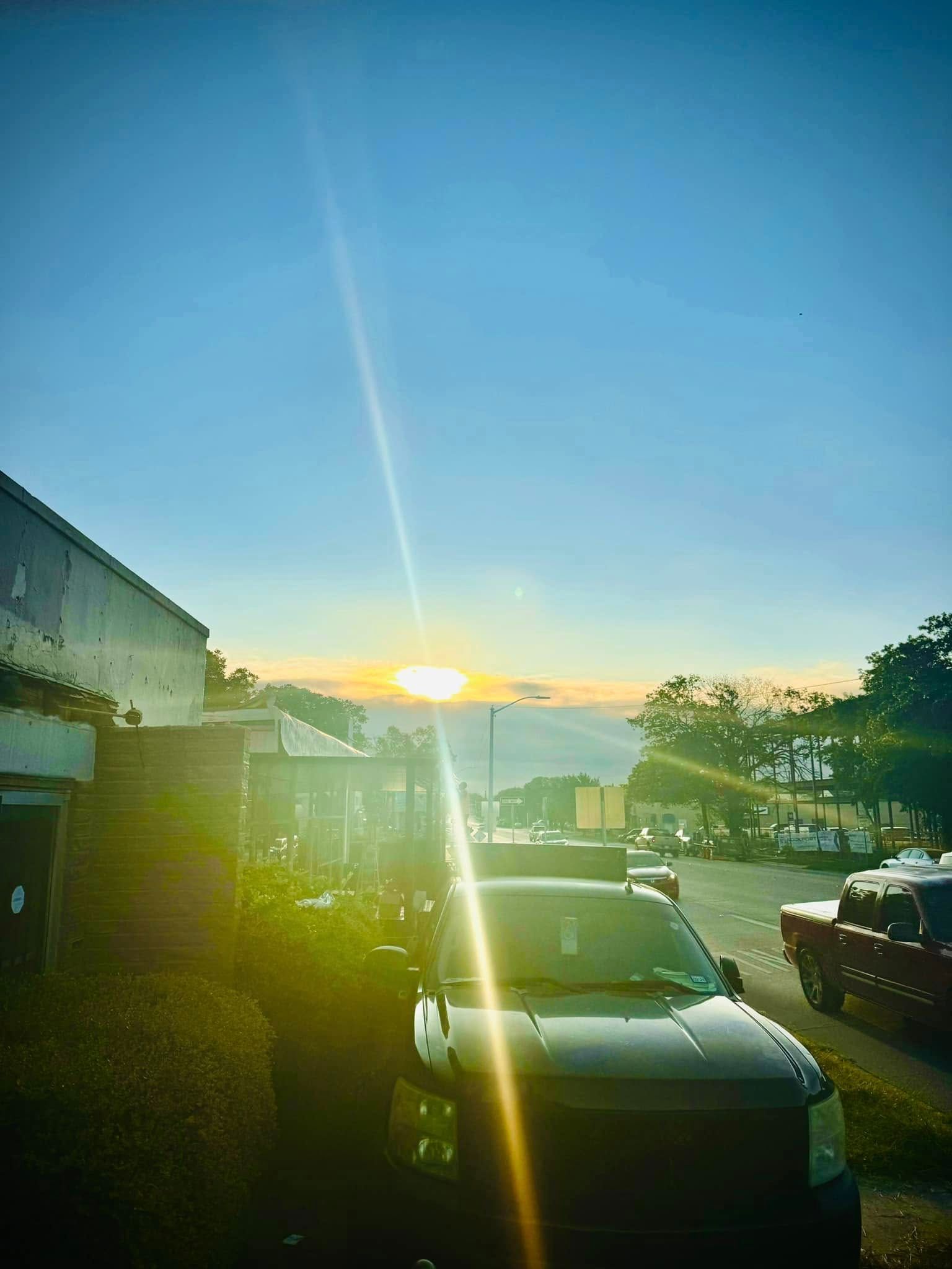A row of cars are parked on the side of the road at sunset.