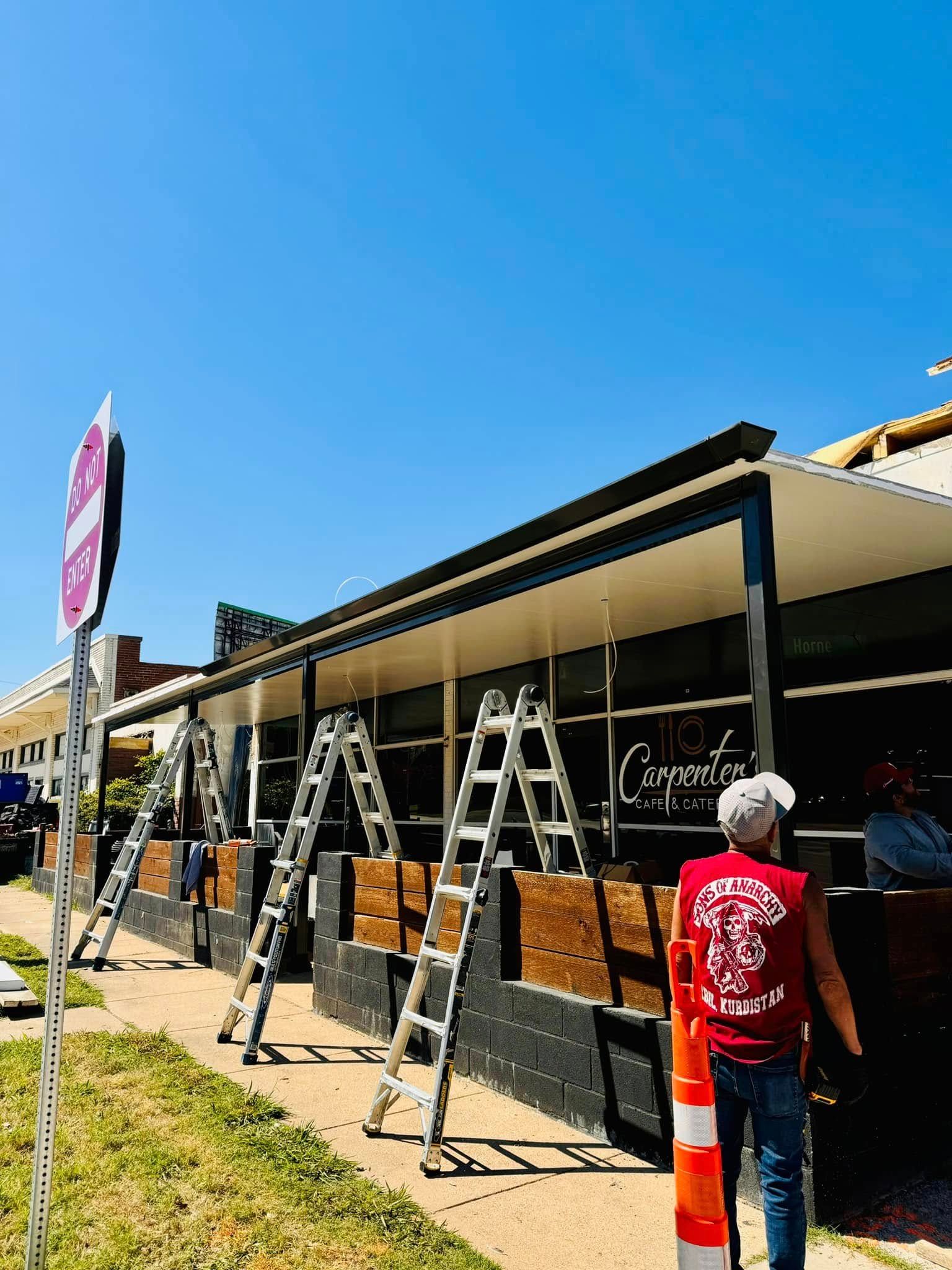 A man in a red shirt is standing in front of a building with ladders.