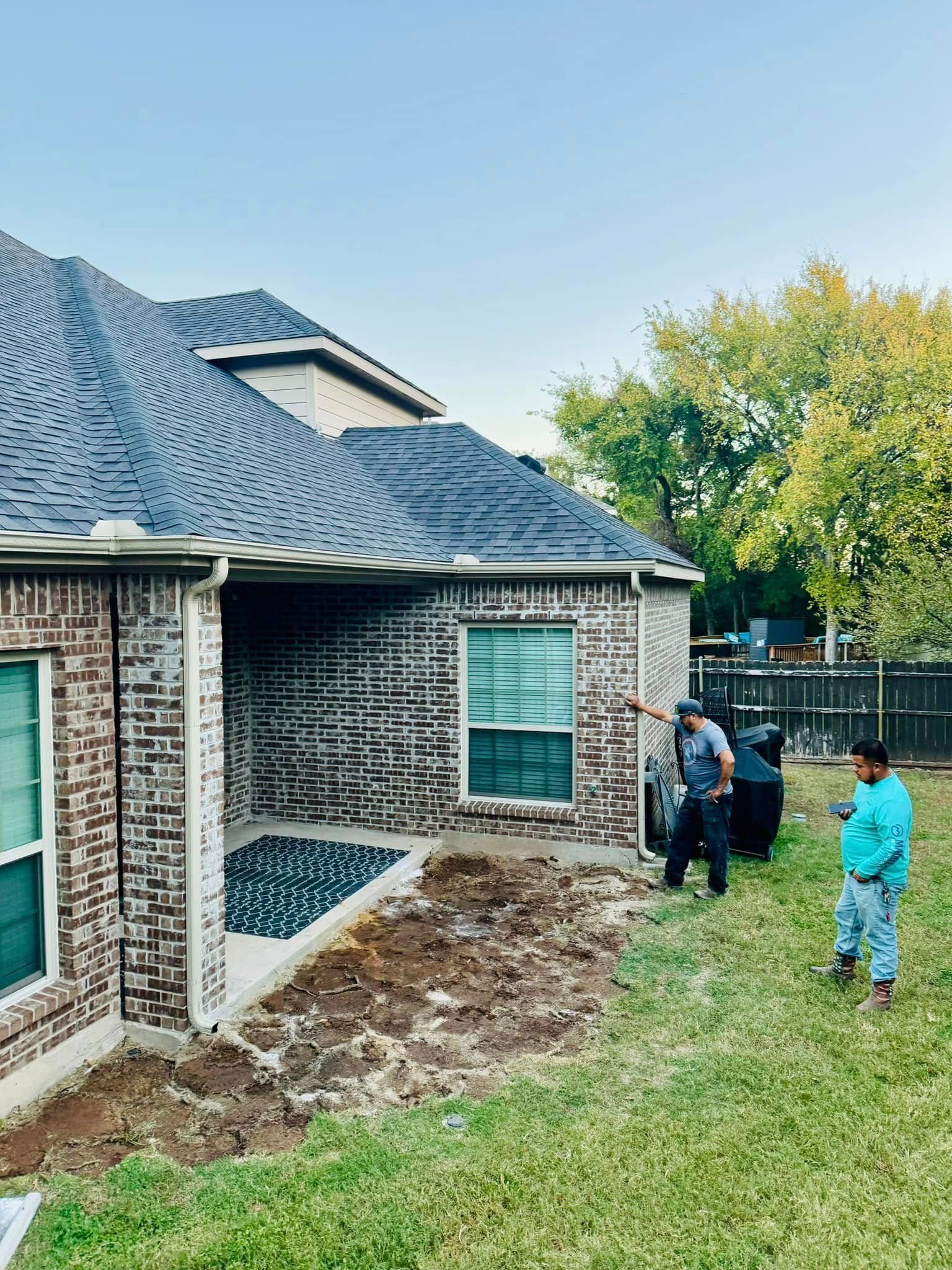 A couple of men are standing in front of a brick house.