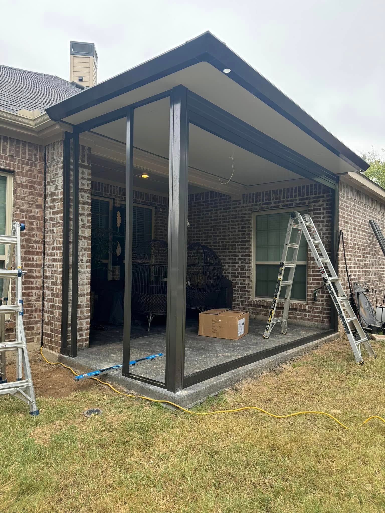A patio cover is being built on the side of a brick house.