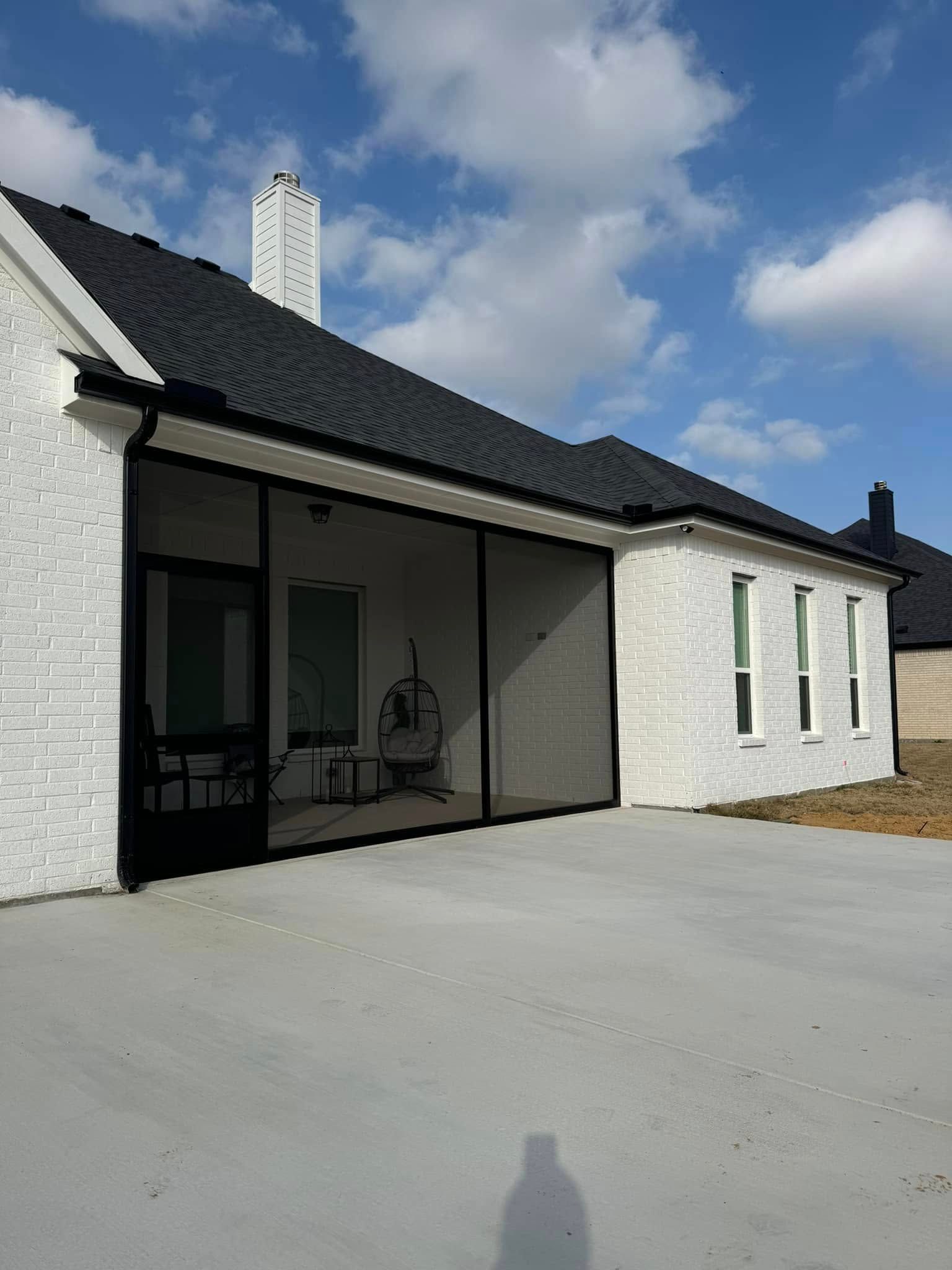 A white house with a black roof and a screened in porch.