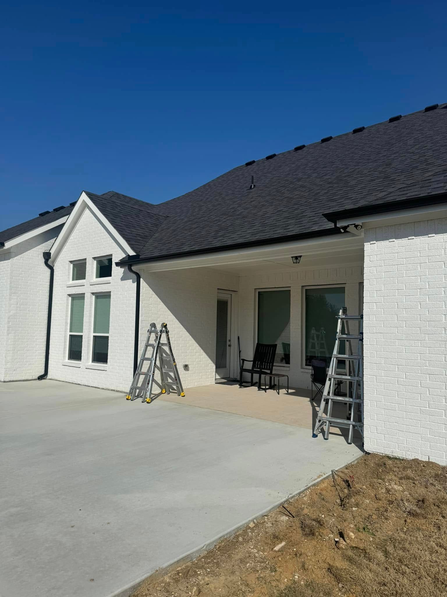 A white house with a black roof and a ladder in front of it.