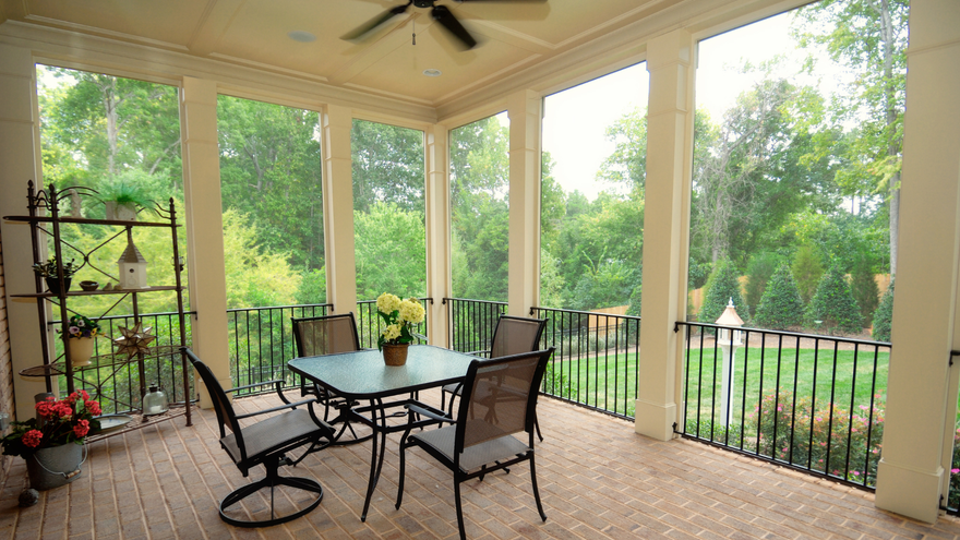 A screened in porch with a table and chairs and a ceiling fan