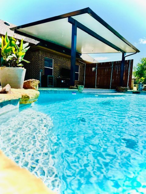 A swimming pool with a canopy over it and a house in the background