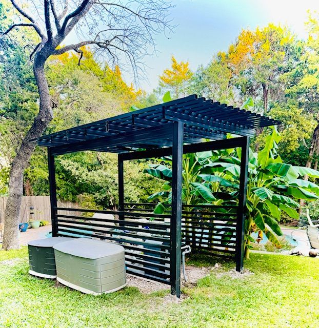 A black pergola is sitting in the middle of a lush green yard.
