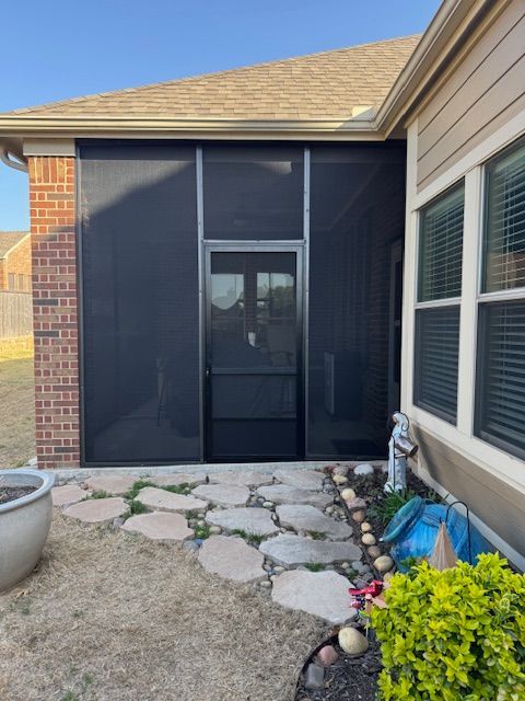 A screened in porch with a brick house in the background