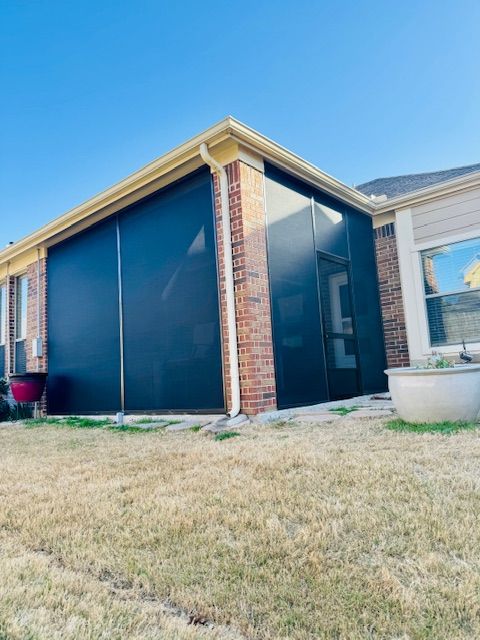 A brick house with a screened in porch and a lawn in front of it.