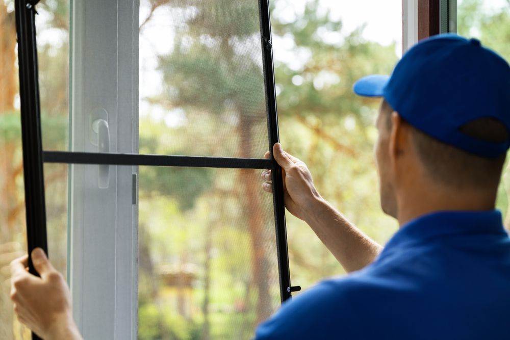 A man in a blue hat is installing a mosquito screen on a window.