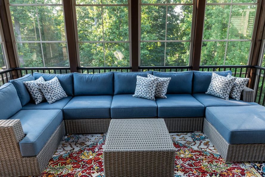A screened in porch with a blue sectional couch and a coffee table.