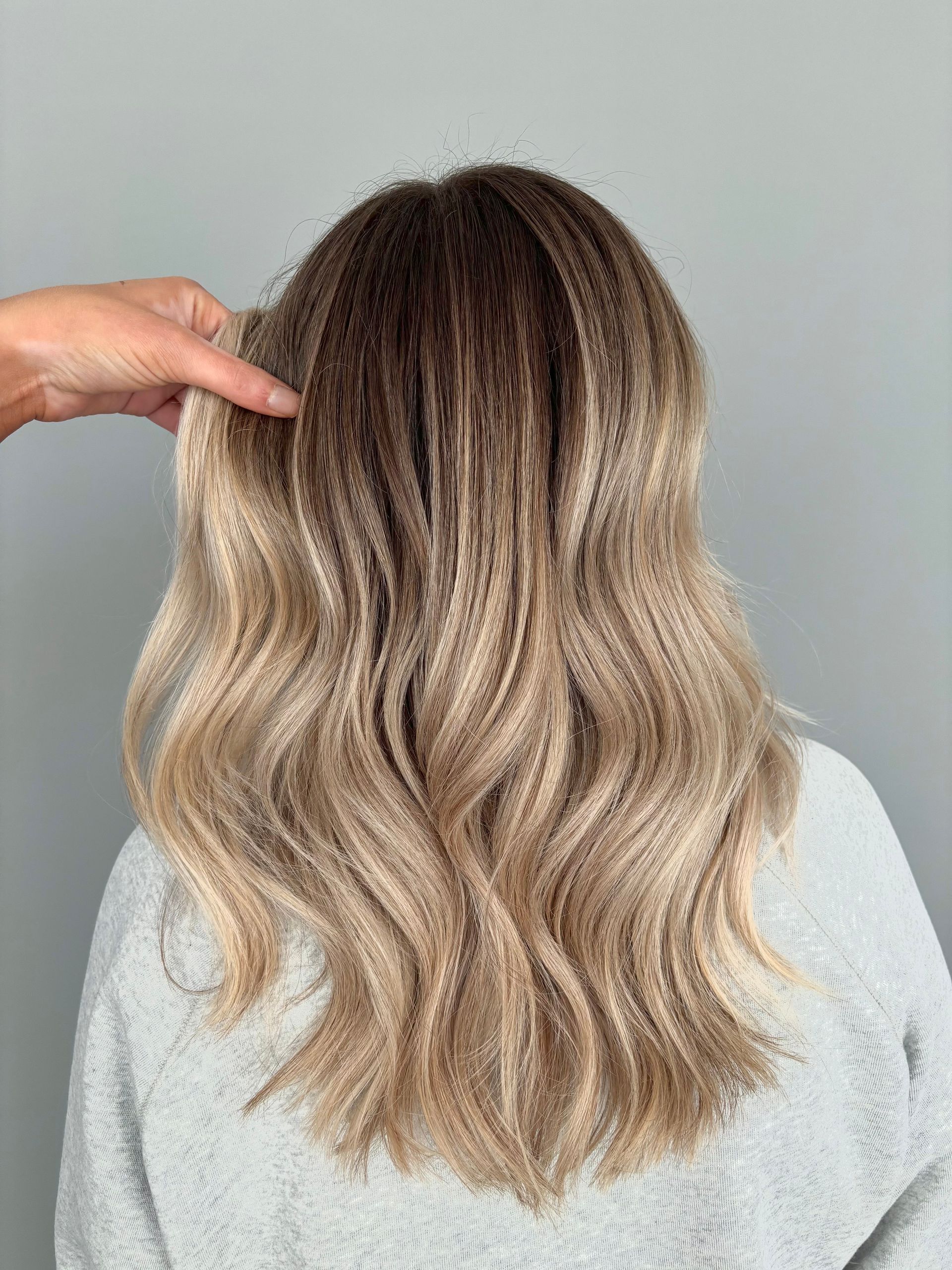 A woman with long wavy blonde hair is getting her hair done by a hairdresser.