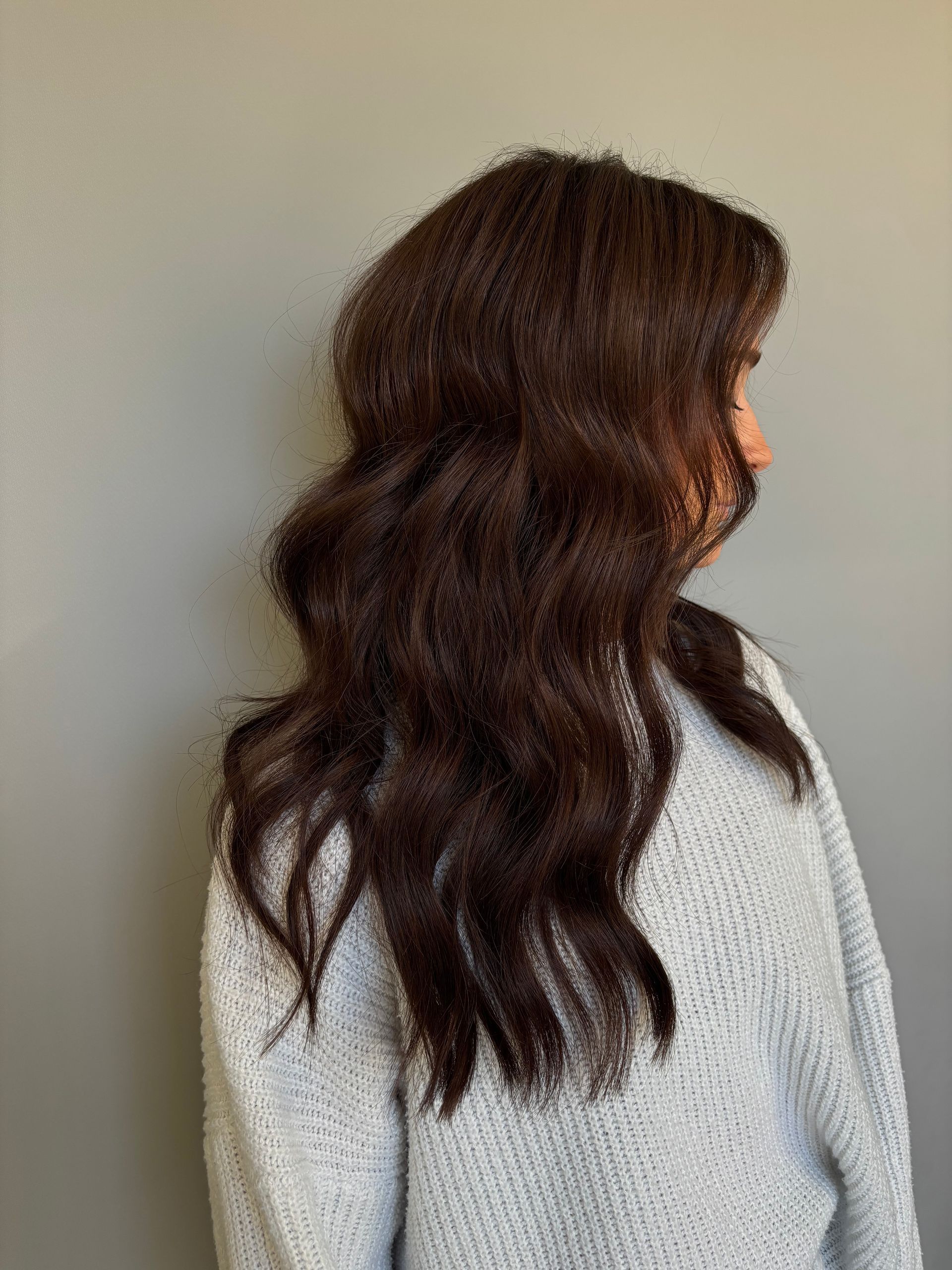 A woman with long brown hair is wearing a grey sweater.