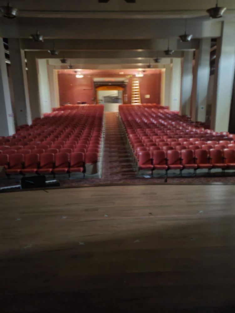A large auditorium with rows of red chairs and a stage