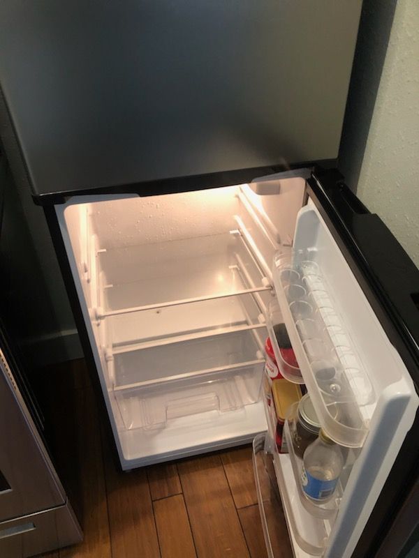 An empty refrigerator with the door open is sitting on a wooden floor