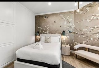 Bedroom with white bedding, floral wallpaper, and a small sofa.