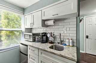 Small kitchen with white cabinets, tile backsplash, sink, and microwave.