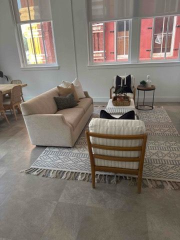 Living room with beige sofa, armchair, rug, and windows with red brick exterior views.
