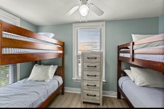 Two bunk beds in a room with blue walls, a white dresser, and a window.