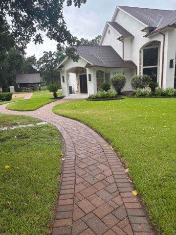 Brick pathway leads to a white house with a dark roof and manicured lawn.