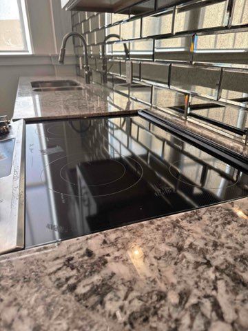 Close-up of a kitchen countertop with an induction cooktop, sink, and mirrored backsplash.