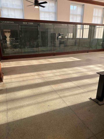 Empty room with a large, glass-fronted information board; tiled floor, windows, and ceiling fan visible.