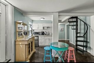 Kitchen with white cabinets, spiral staircase, and teal table with stools.