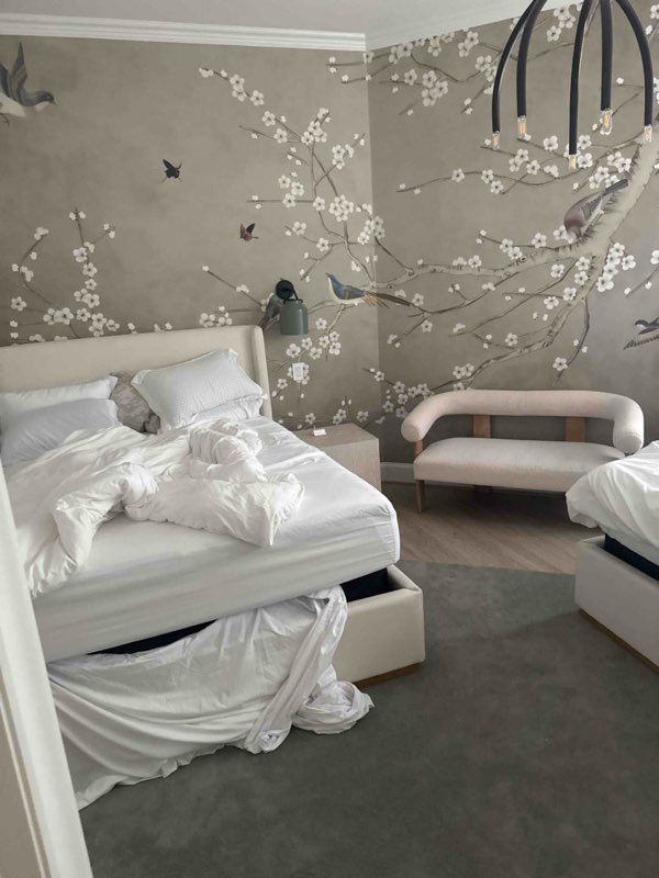 Bedroom with white bedding, floral wallpaper, small sofa, and gray carpet.