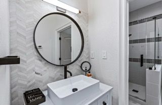 Modern bathroom with round mirror, vessel sink, herringbone tile, and shower stall.