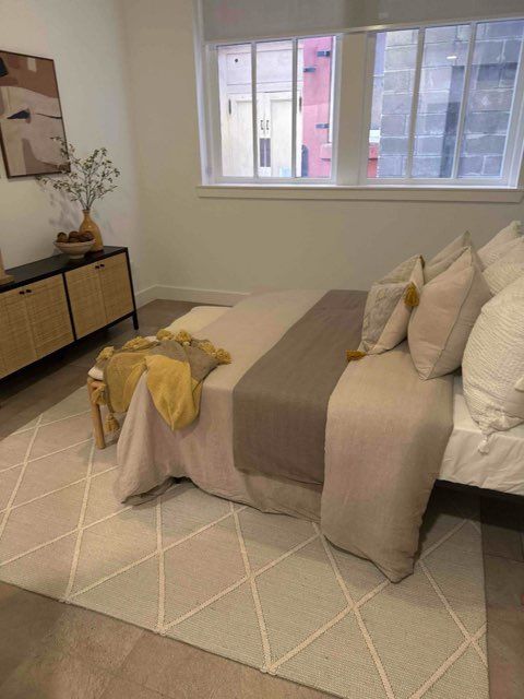 Bedroom with bed, rug, and cabinet. Neutral tones with accents of yellow and brown.