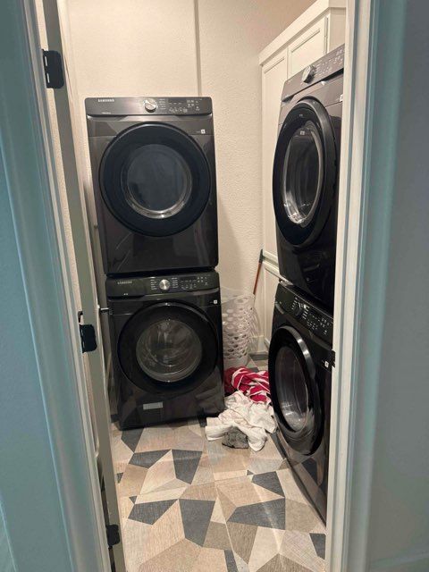 Laundry room with two stacked dark washers and dryers, messy floor.