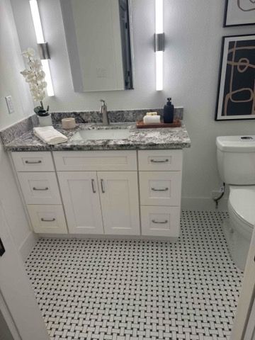 White bathroom with floating vanity, patterned floor, and artwork.