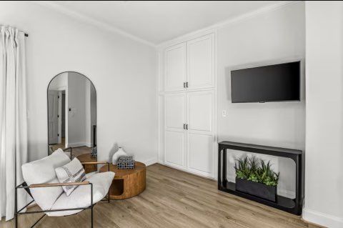 A modern living space with a white chair, arched mirror, wooden coffee table, built-in storage, and a TV.