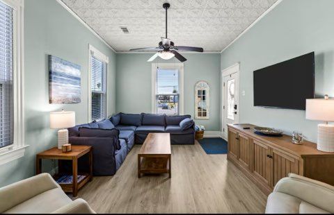 Living room with blue sectional sofa, TV, and wooden furniture; light blue walls, and patterned ceiling.
