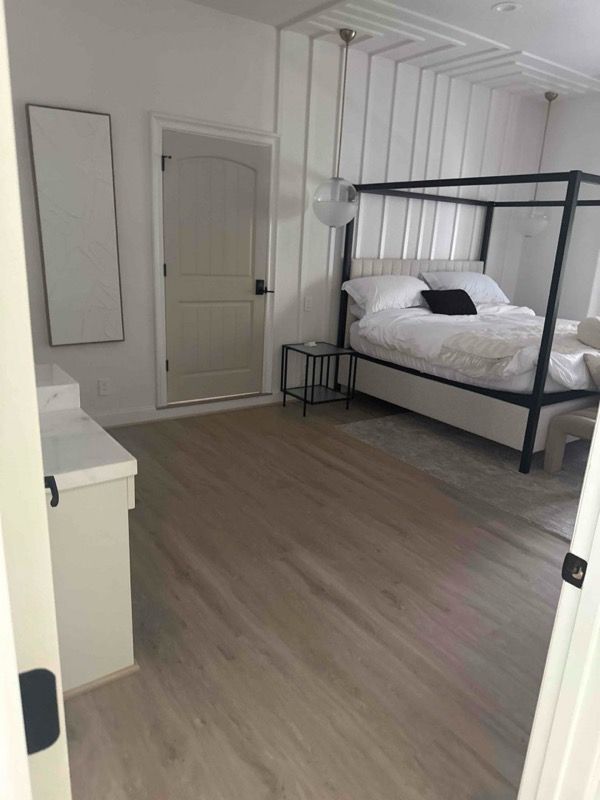 Bedroom with a black canopy bed, white walls, and light wood flooring.