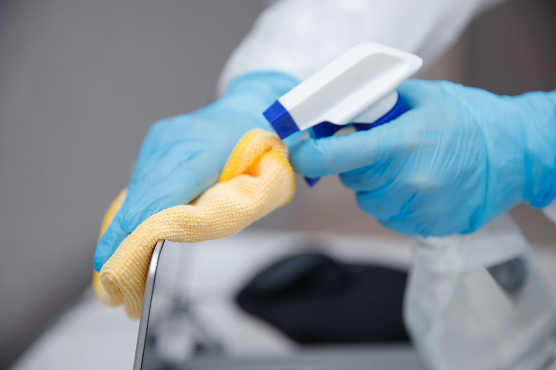 A person wearing blue gloves is cleaning a sink with a cloth and spray bottle