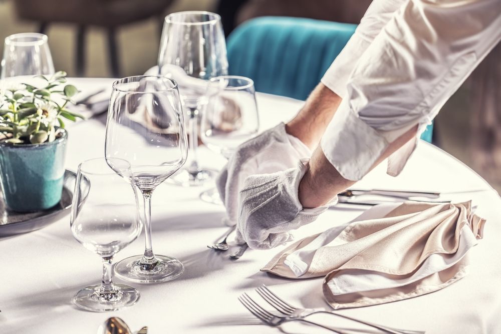 Server setting a restaurant table with white gloves.