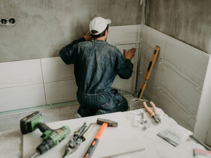 A man is installing tiles on a wall in a bathroom.