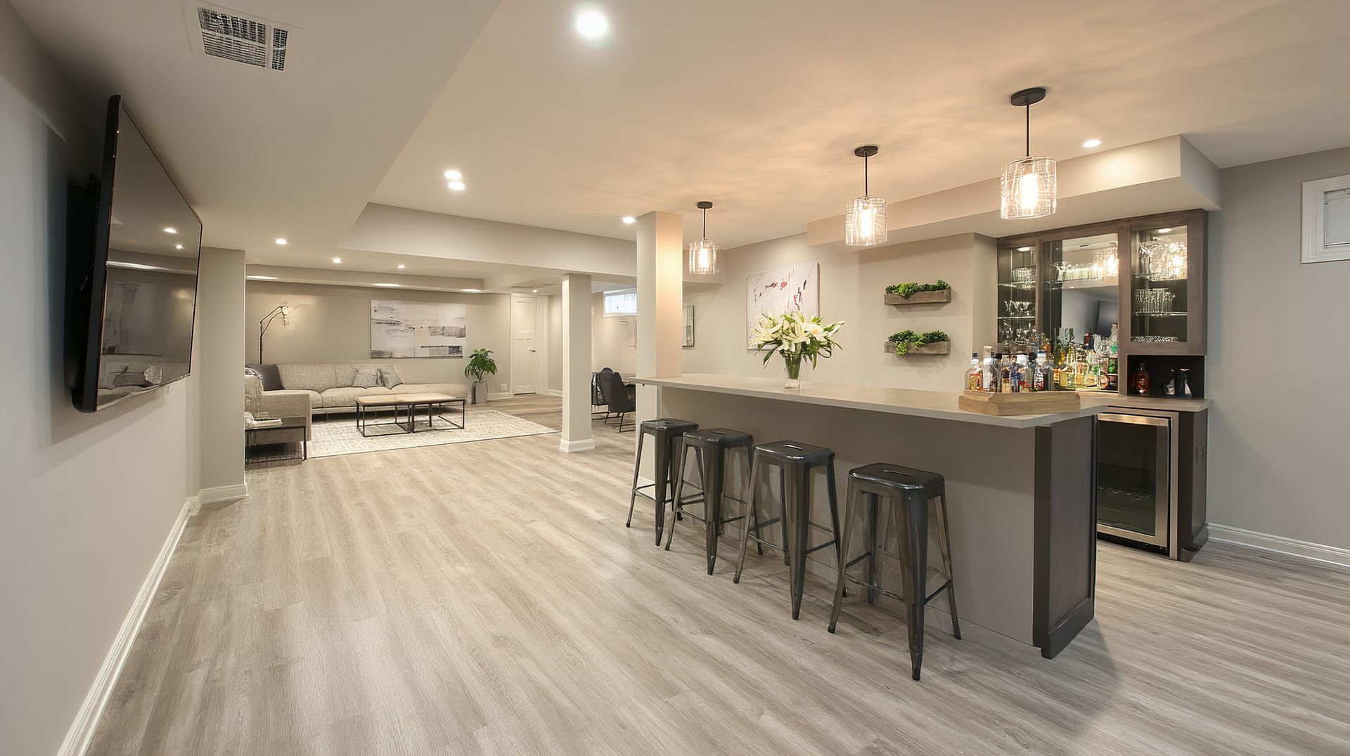 Modern open-concept basement kitchen and bar with island seating, light wood floors, and recessed lighting