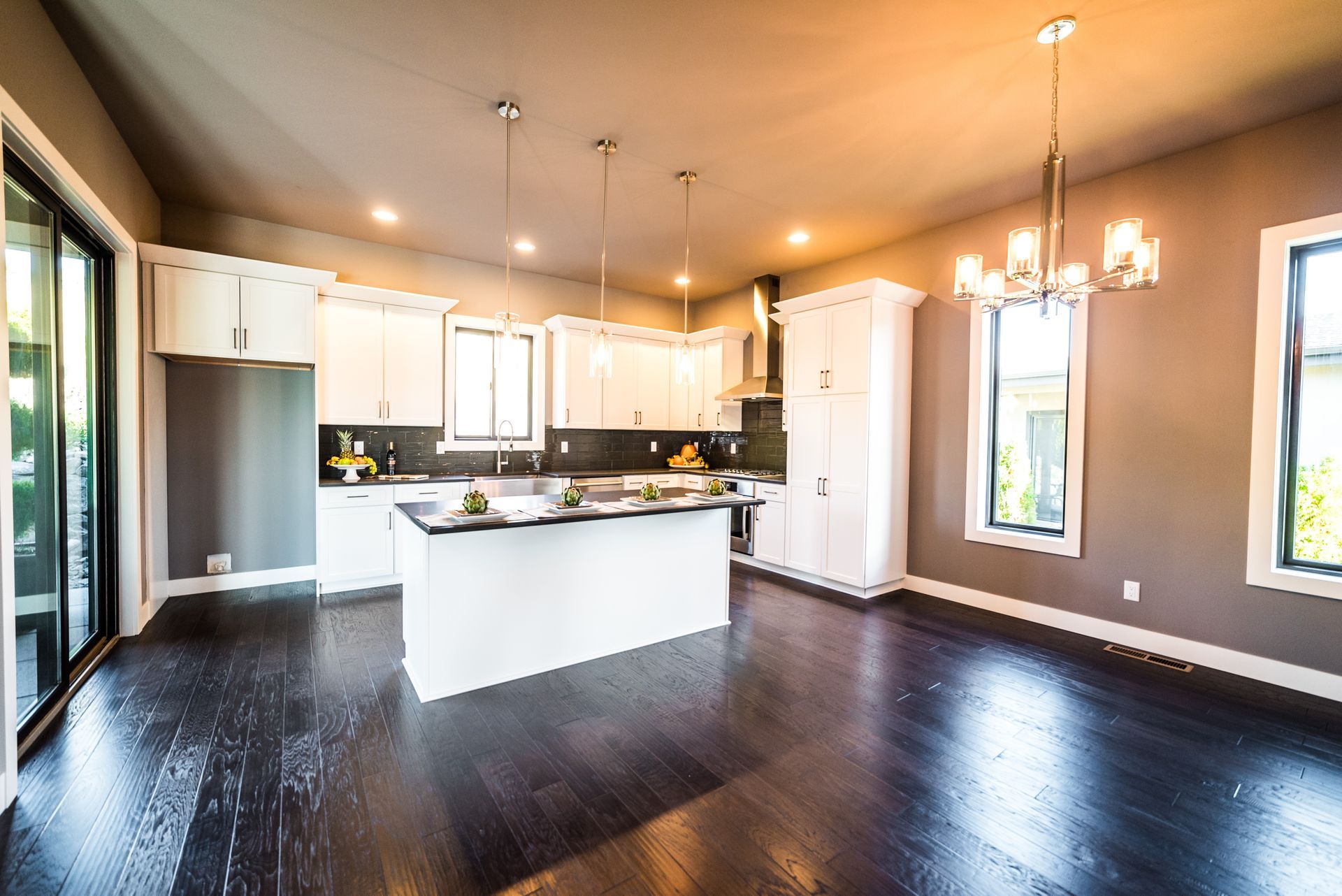 Bright open kitchen with dark hardwood floors, white cabinets, a large island, and pendant lighting
