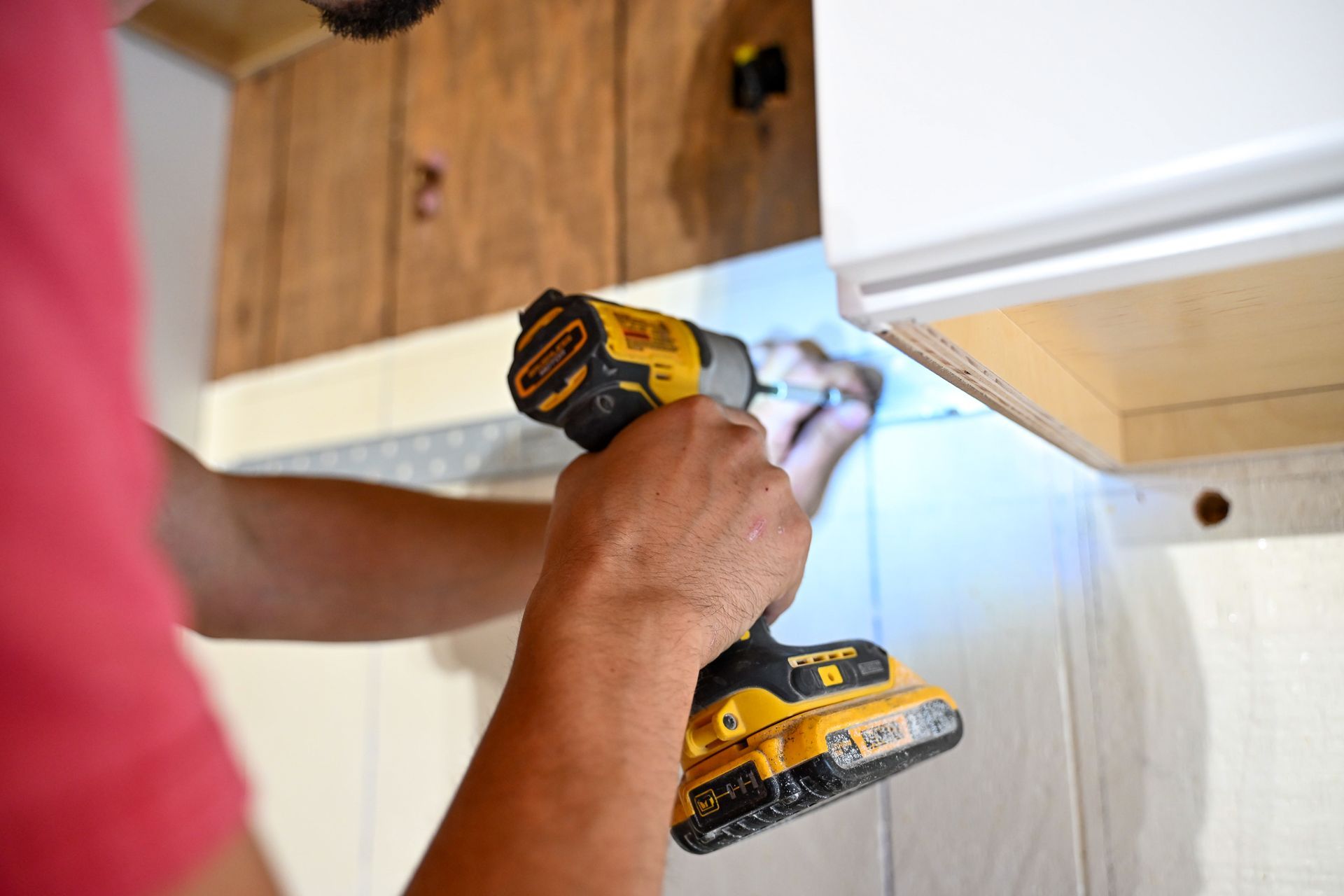 Person using a yellow and black drill to install a white cabinet.