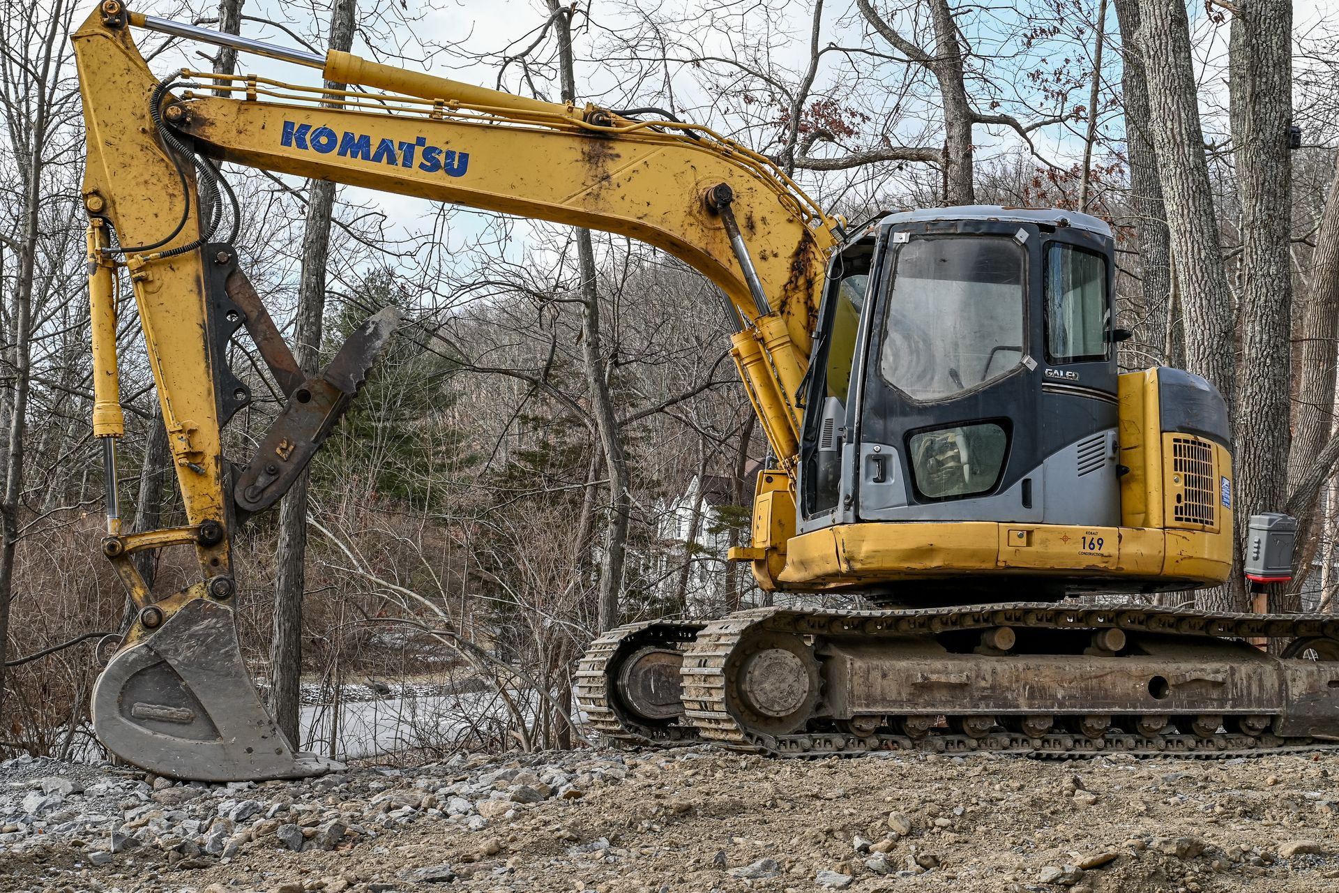 Yellow Komatsu excavator on a construction site; dirt and trees in the background.