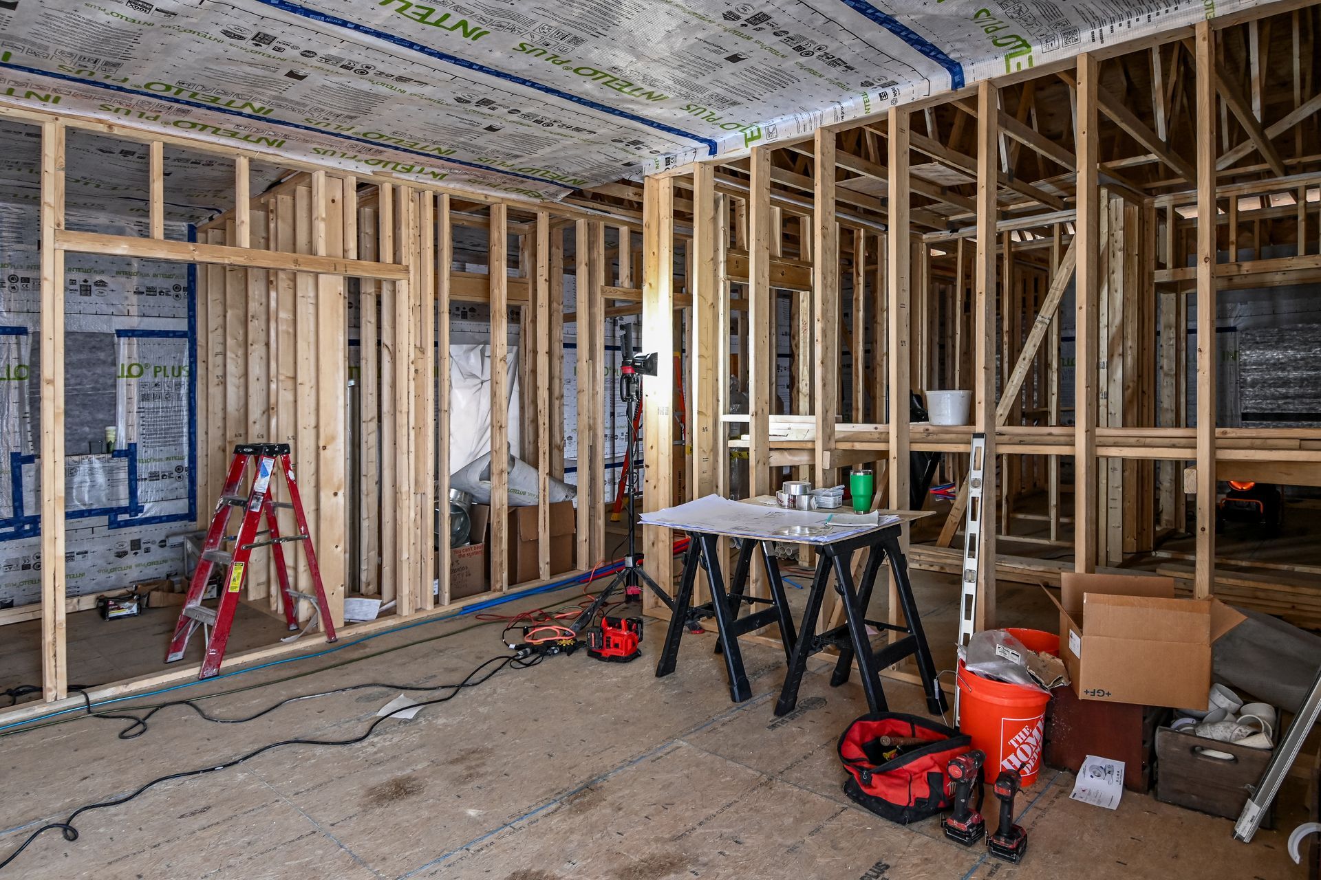 Interior view of a building under construction, showing wooden framing, tools, and a red ladder.