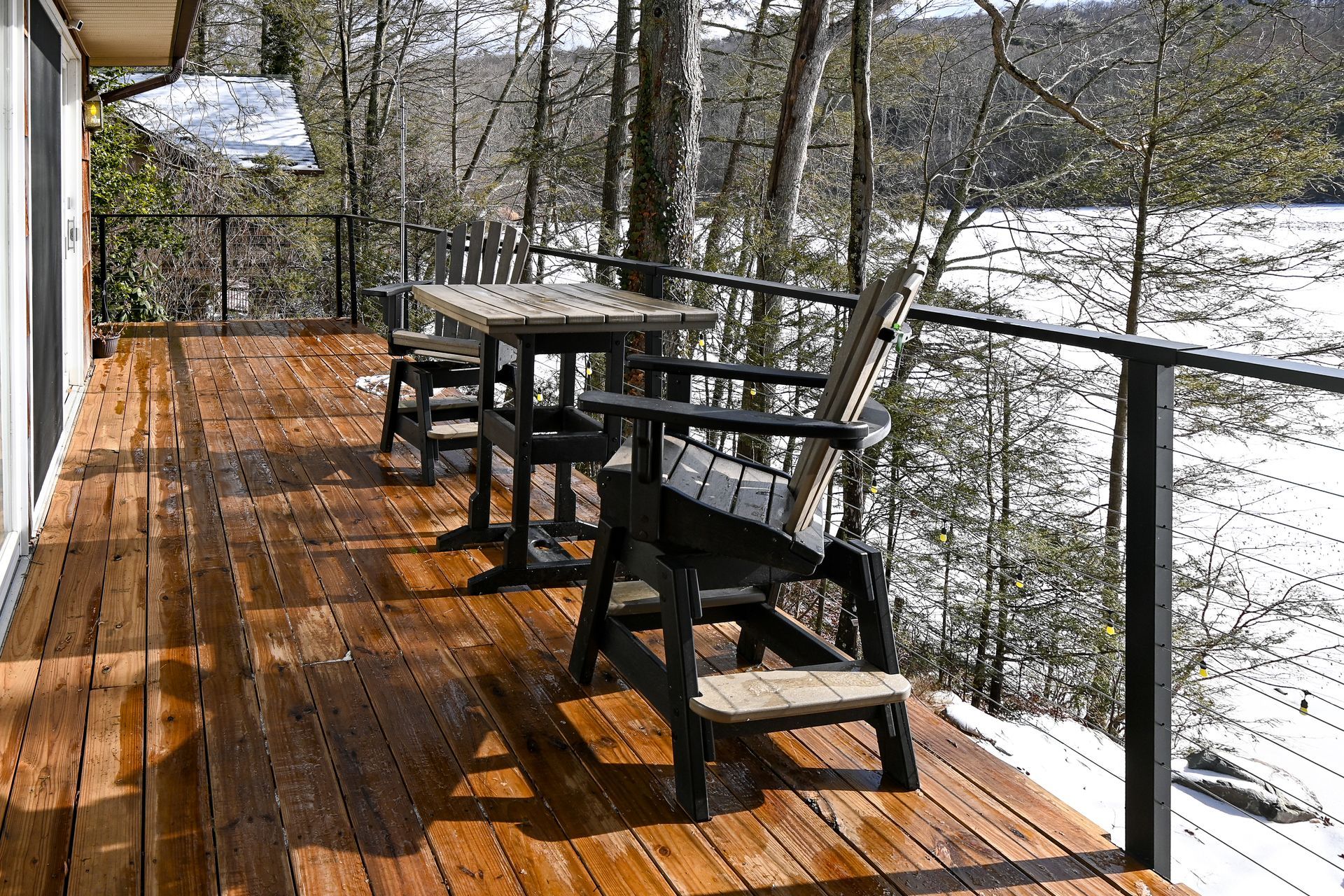 Wooden deck with table and chairs overlooking a snowy landscape and water.