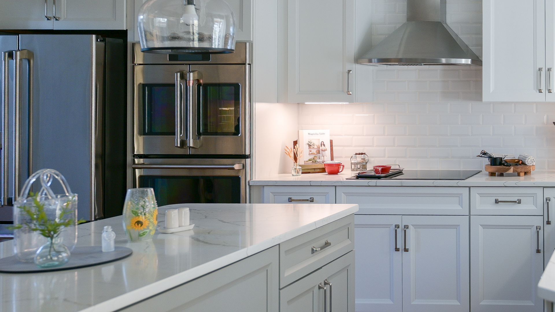There is a large island in the middle of the kitchen. Modern white kitchen with stainless steel appliances, white cabinets, and island with marble countertop.