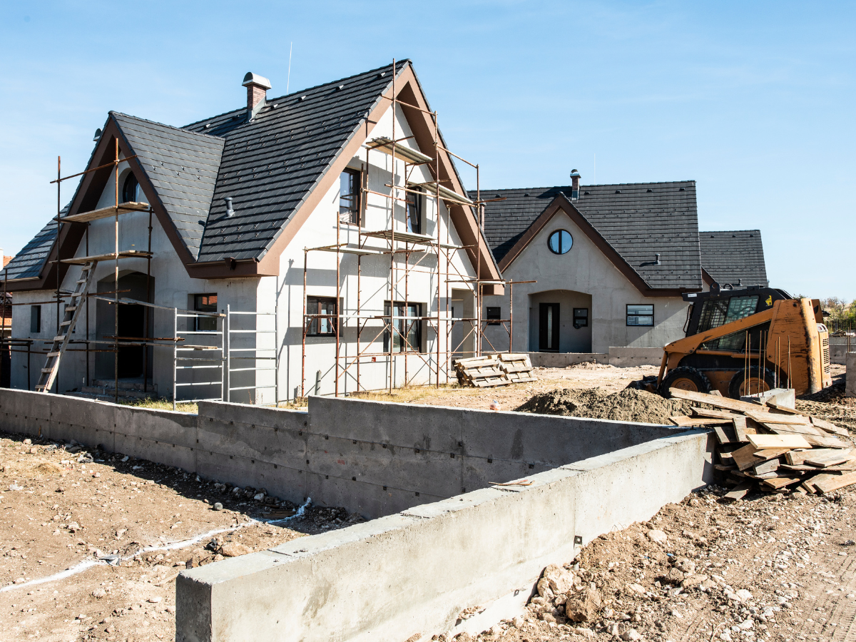 A house is being built with scaffolding and a bulldozer in the background. A house is being built with scaffolding and a bulldozer in the background.