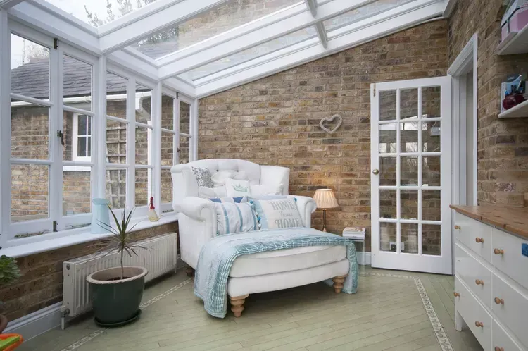 A conservatory with a couch , chair , and lots of windows.