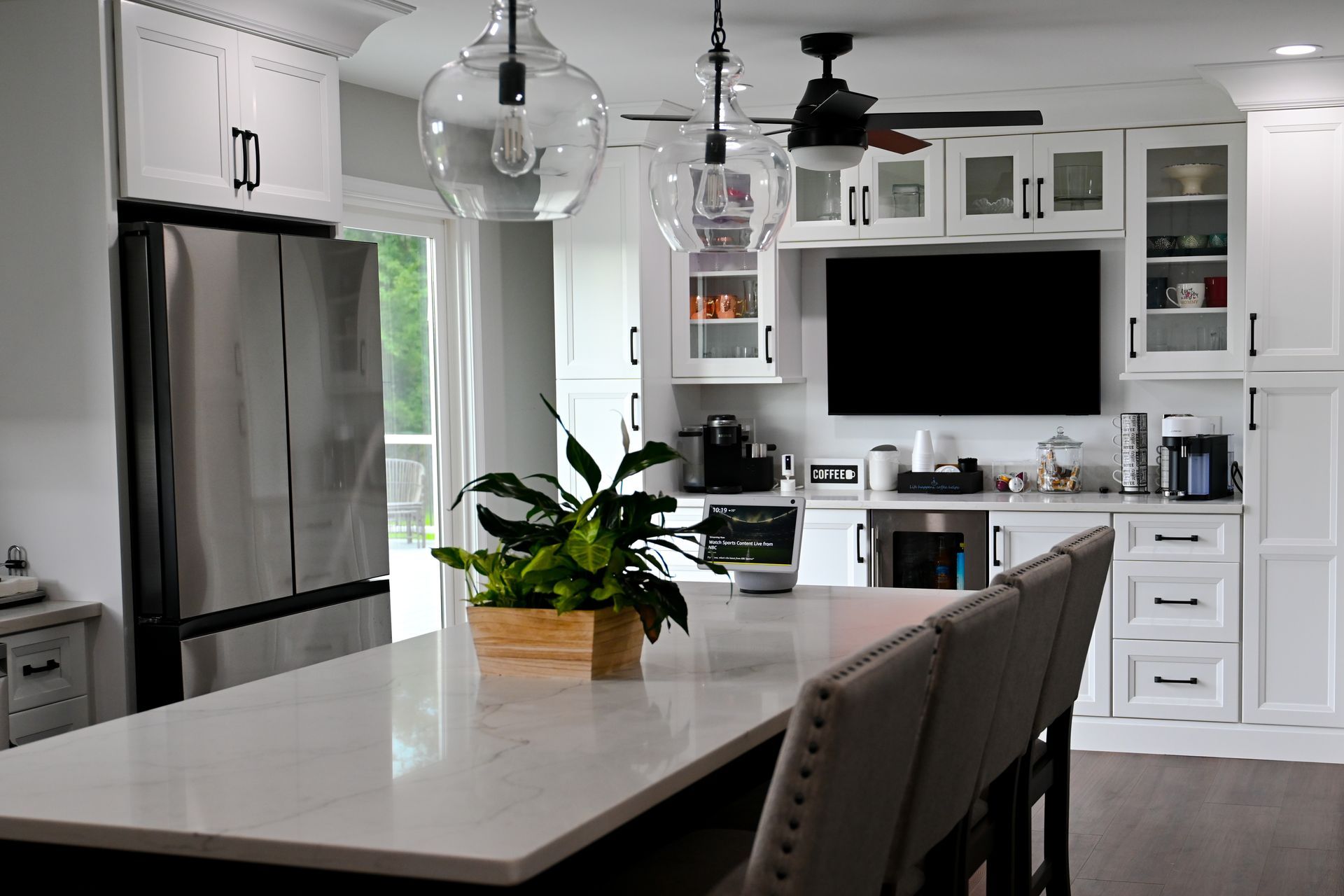 A kitchen with white cabinets , stainless steel appliances , a large island , and a flat screen tv.