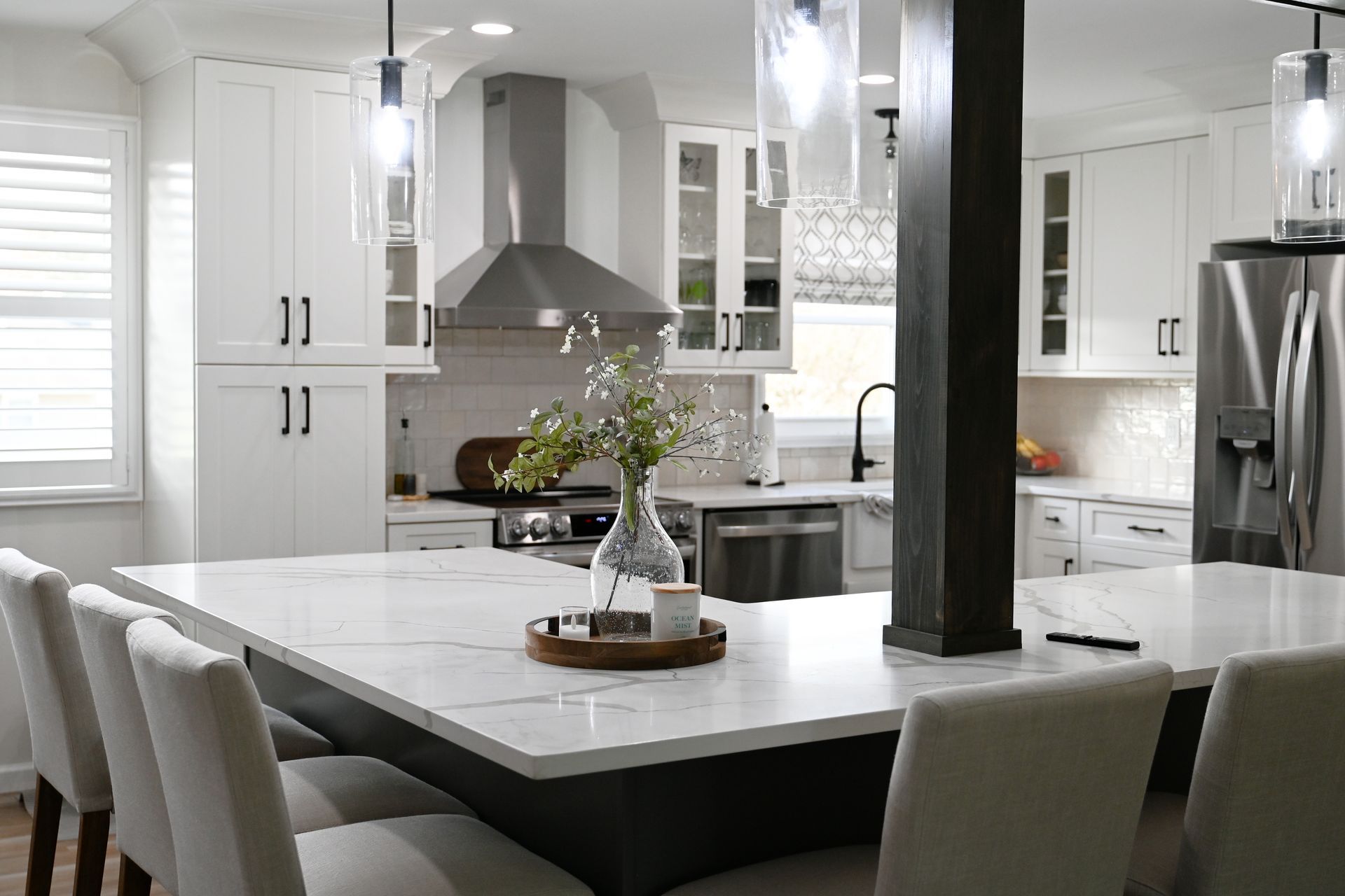 Modern kitchen with white cabinets, large island with seating, stainless steel appliances, and hanging lights.