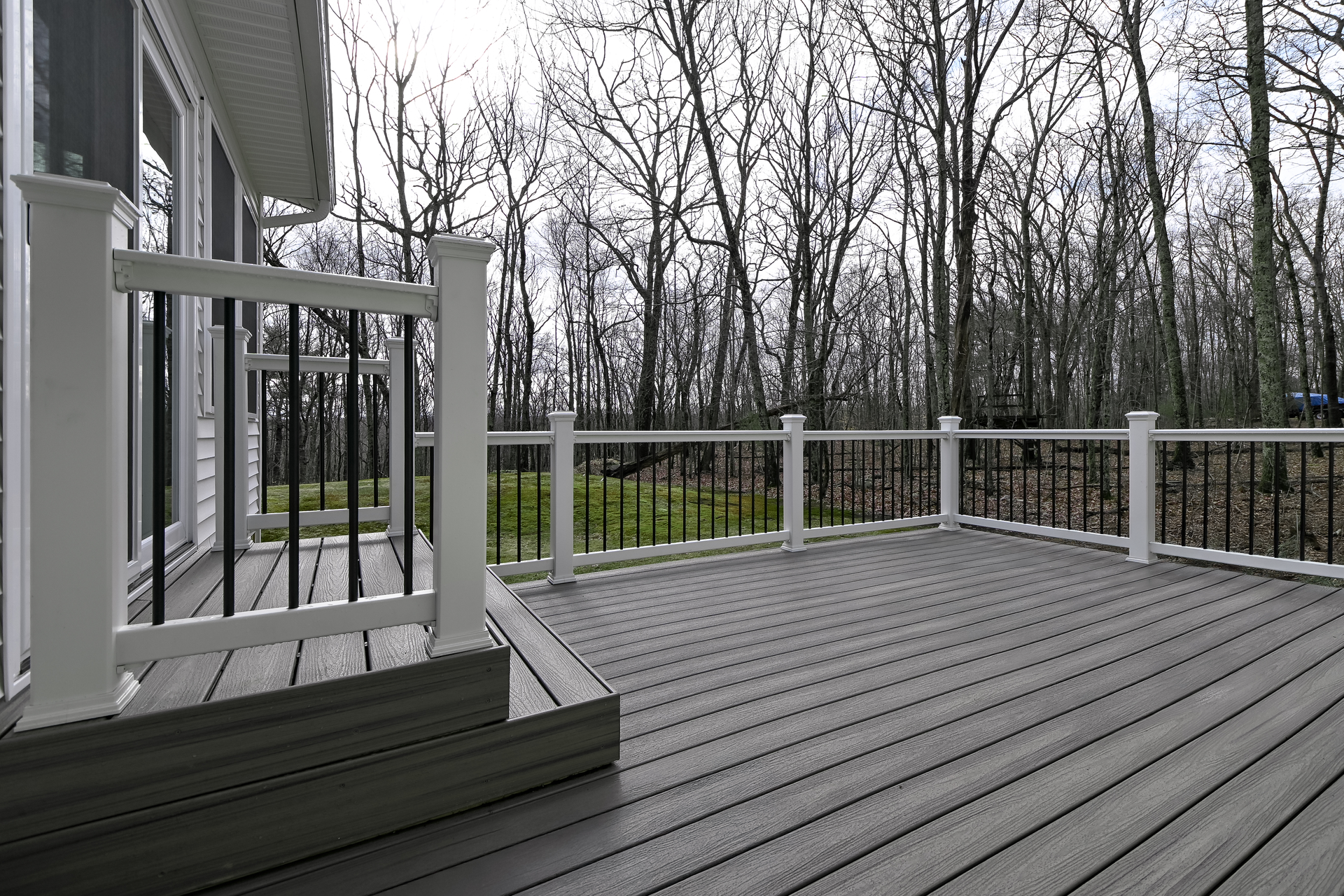 Gray composite deck with white posts and black railings, overlooking a wooded area. Gray composite deck with white posts and black railings, overlooking a wooded area.