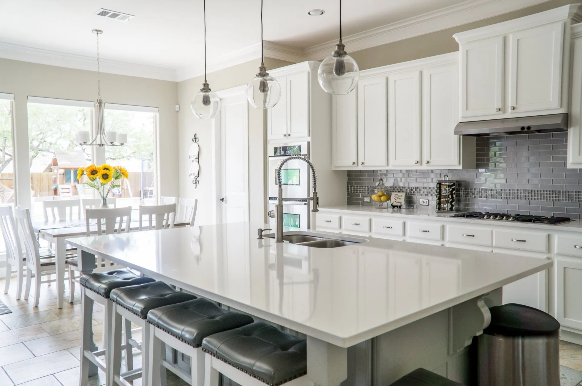 White kitchen with island, seating, and overhead lights; dining area visible through windows.