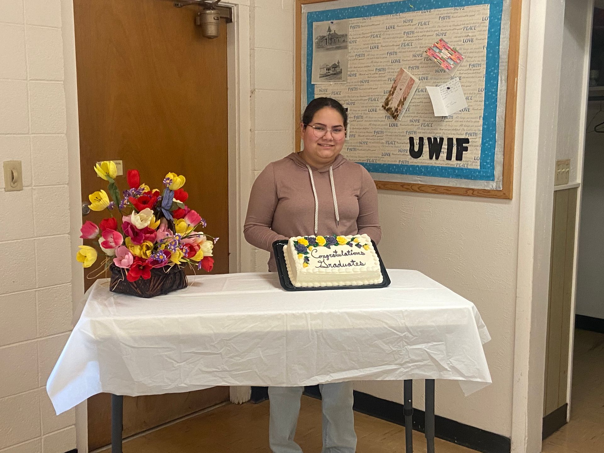 Person standing behind a table with flowers and a decorated cake in a hallway display area